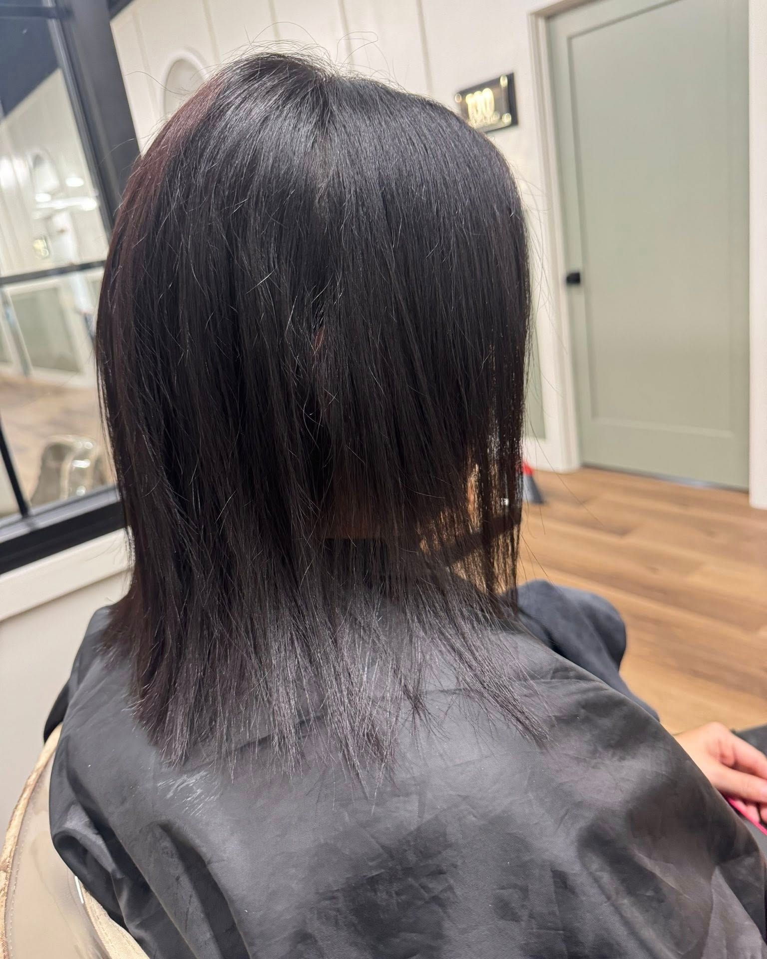 Person with dark, straight hair, viewed from the back, in a salon. Hair is below the shoulders.