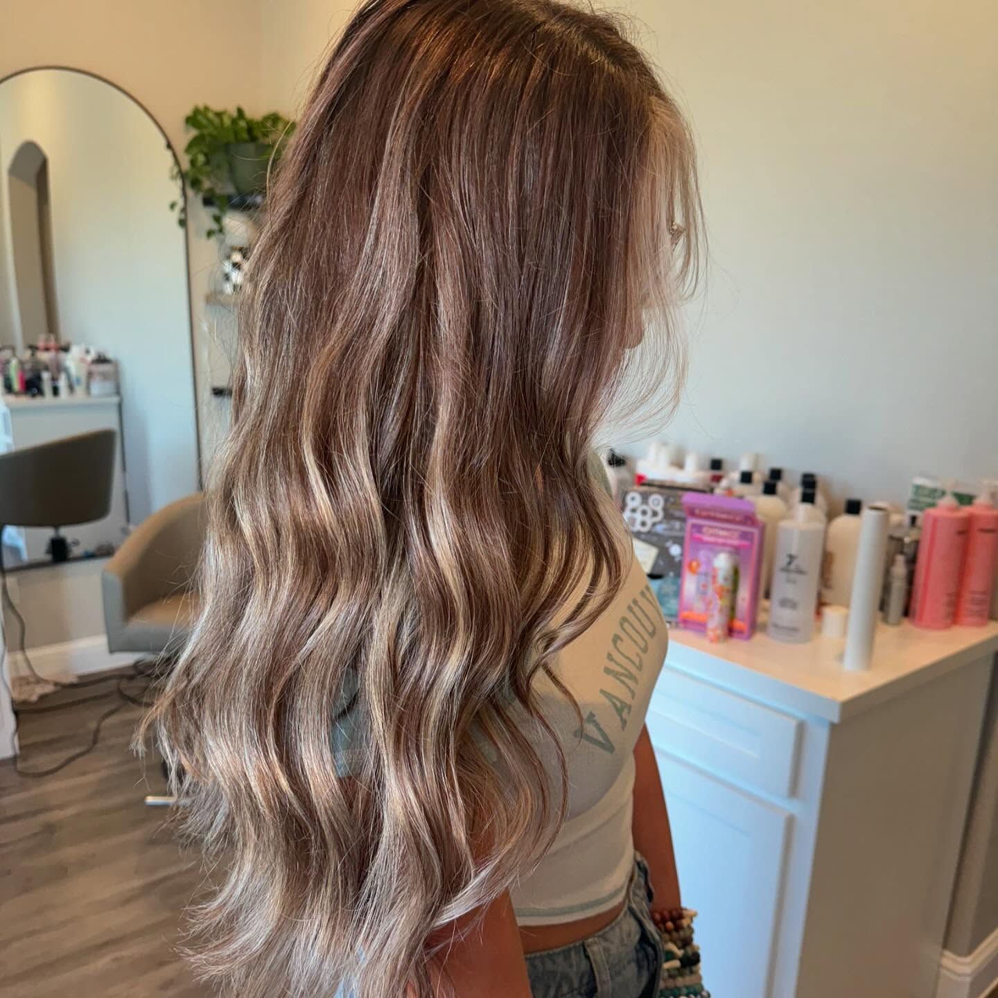Woman with long, wavy brown and blonde highlighted hair in a salon.