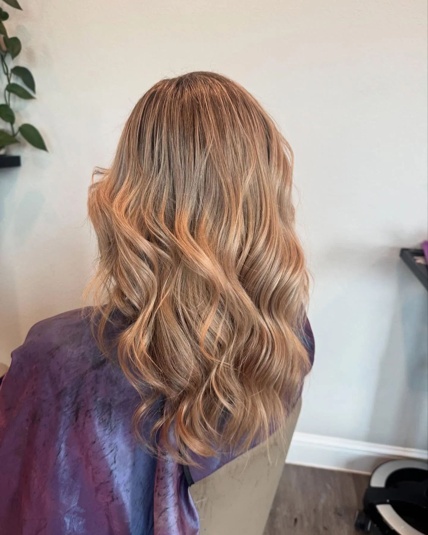 Woman with wavy, crimped light brown hair. She wears a purple salon cape.