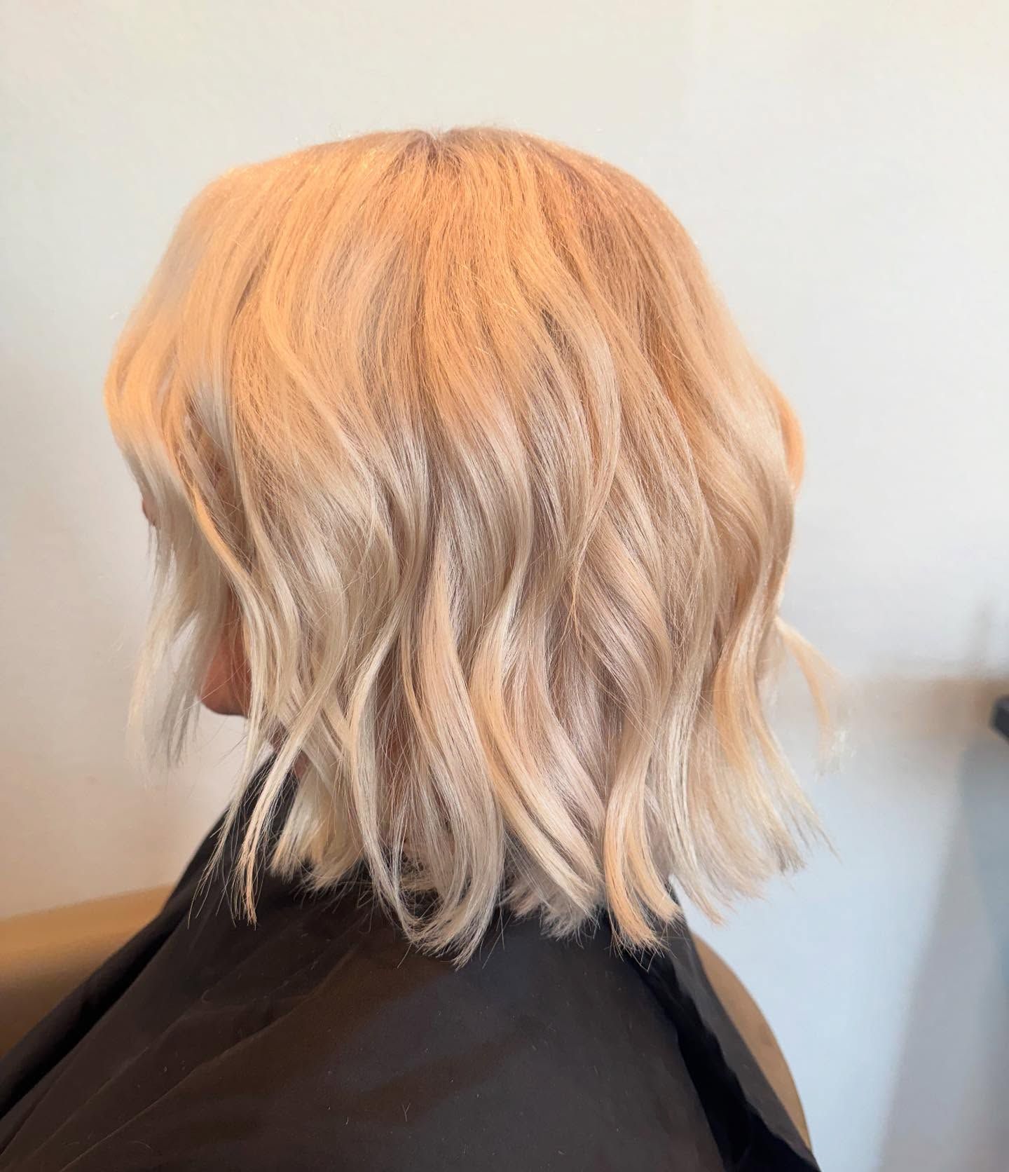 Blonde bob haircut with loose waves, against a white wall.