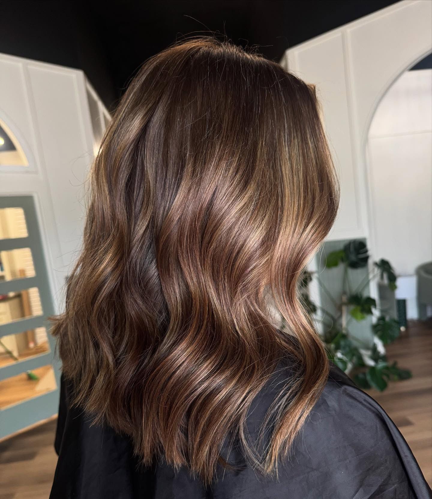 Woman with wavy, dark brown hair with highlights in a salon setting.