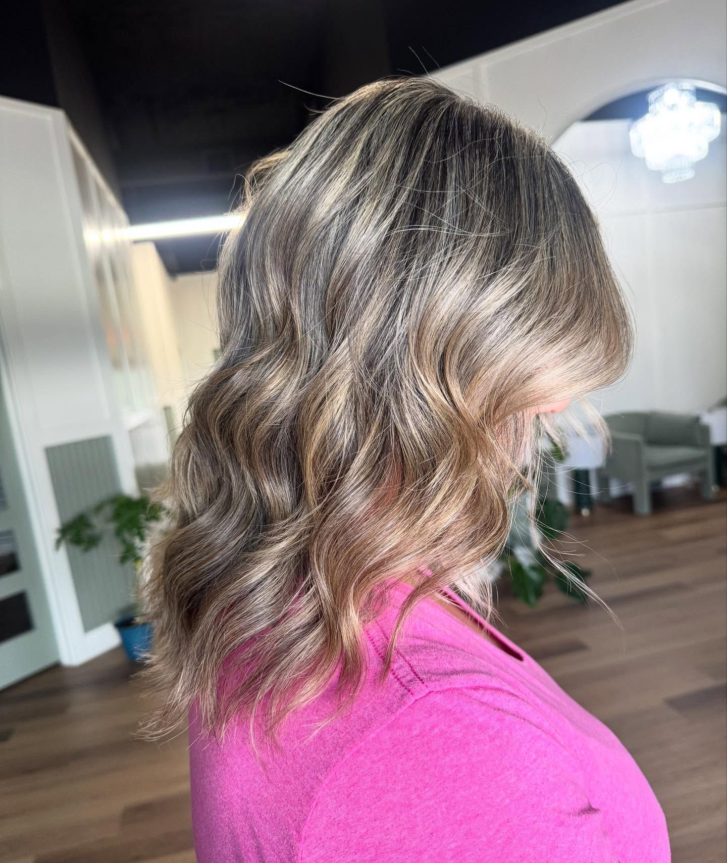 Woman with wavy, highlighted hair; wearing a pink shirt.