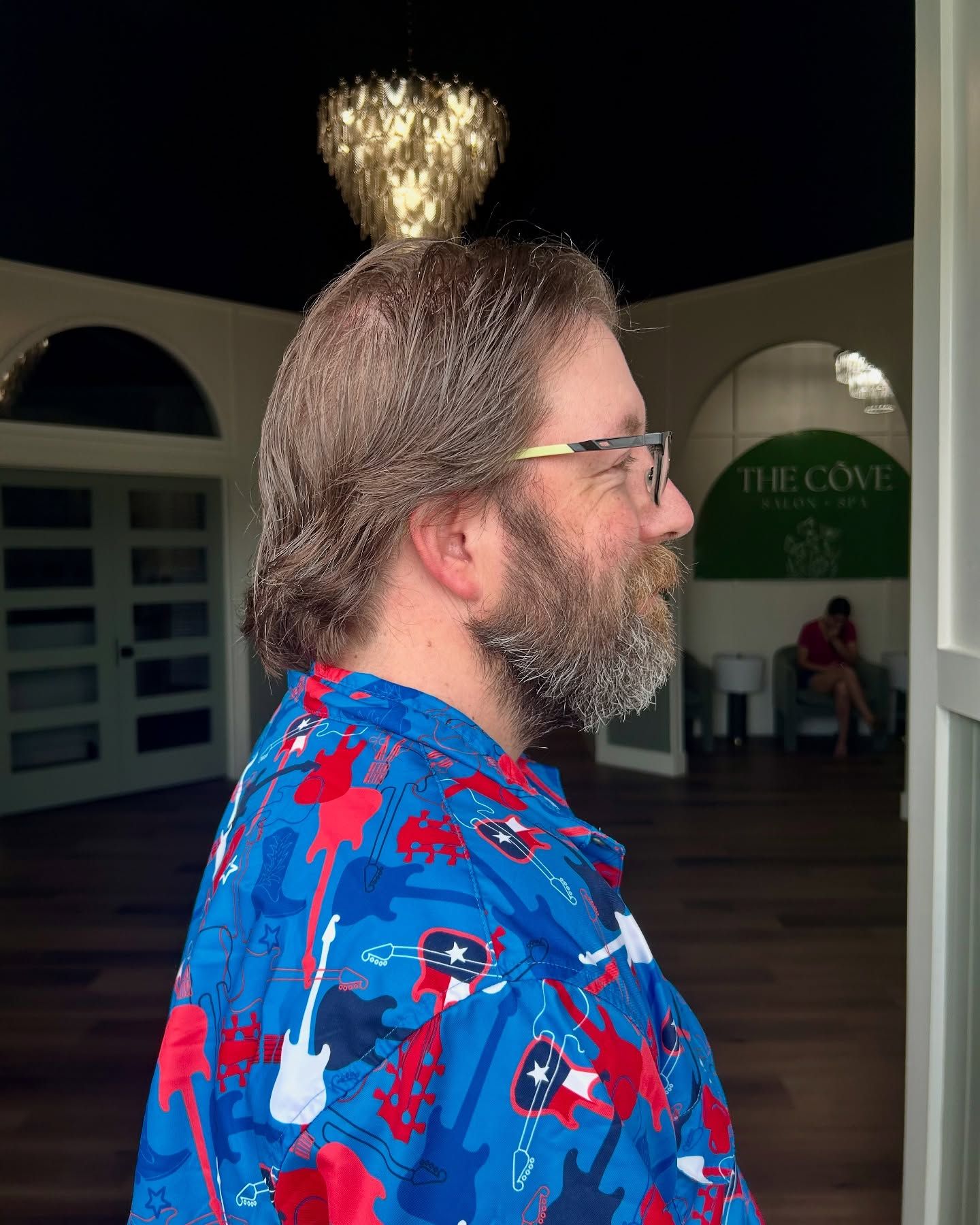 Man with glasses and beard, wearing a patterned blue shirt, stands indoors.