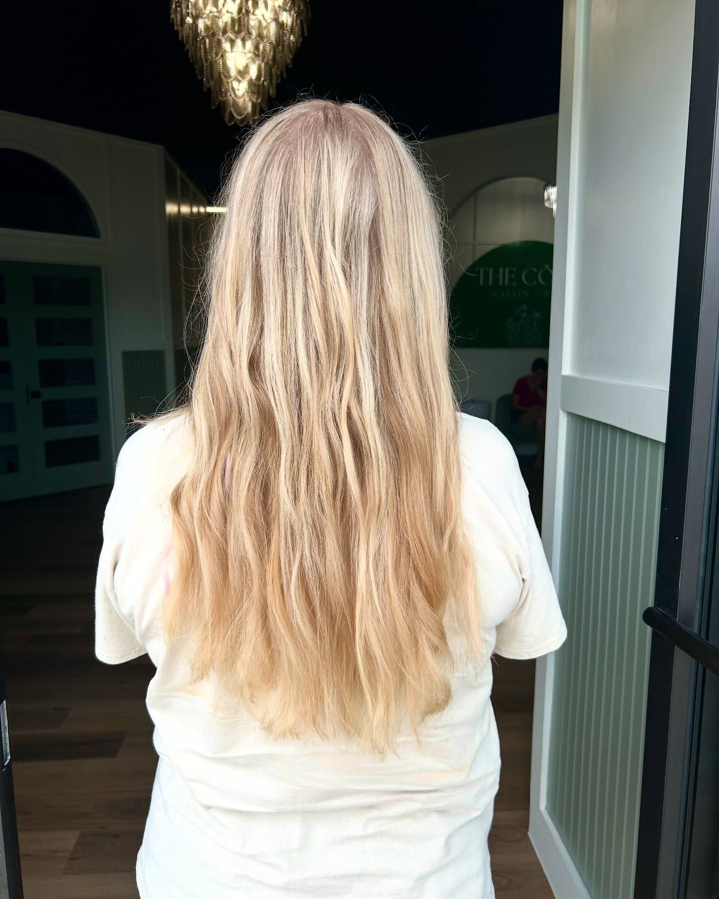 Woman with long, light-colored, wavy hair stands near a doorway.