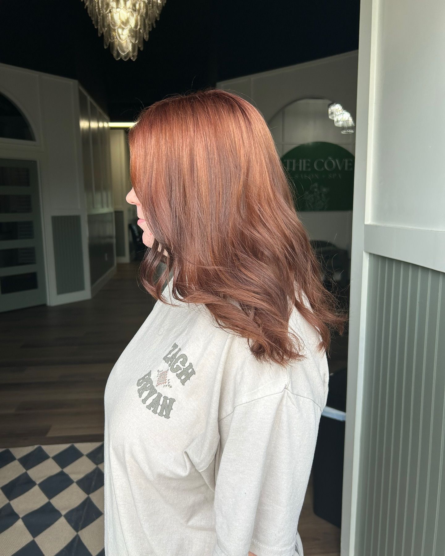 Woman with auburn hair in a tan sweatshirt stands inside a building.
