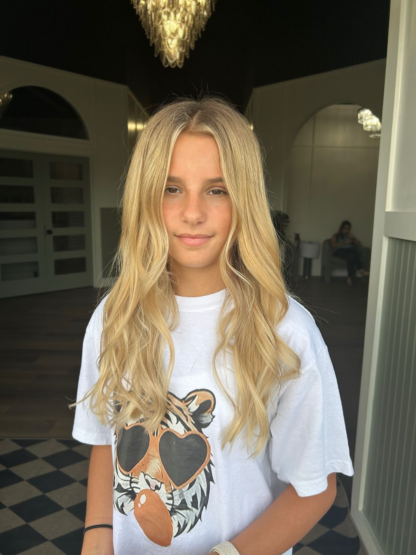 Blonde-haired person wearing a white t-shirt with a heart-eyed tiger design, standing indoors, looking at the camera.