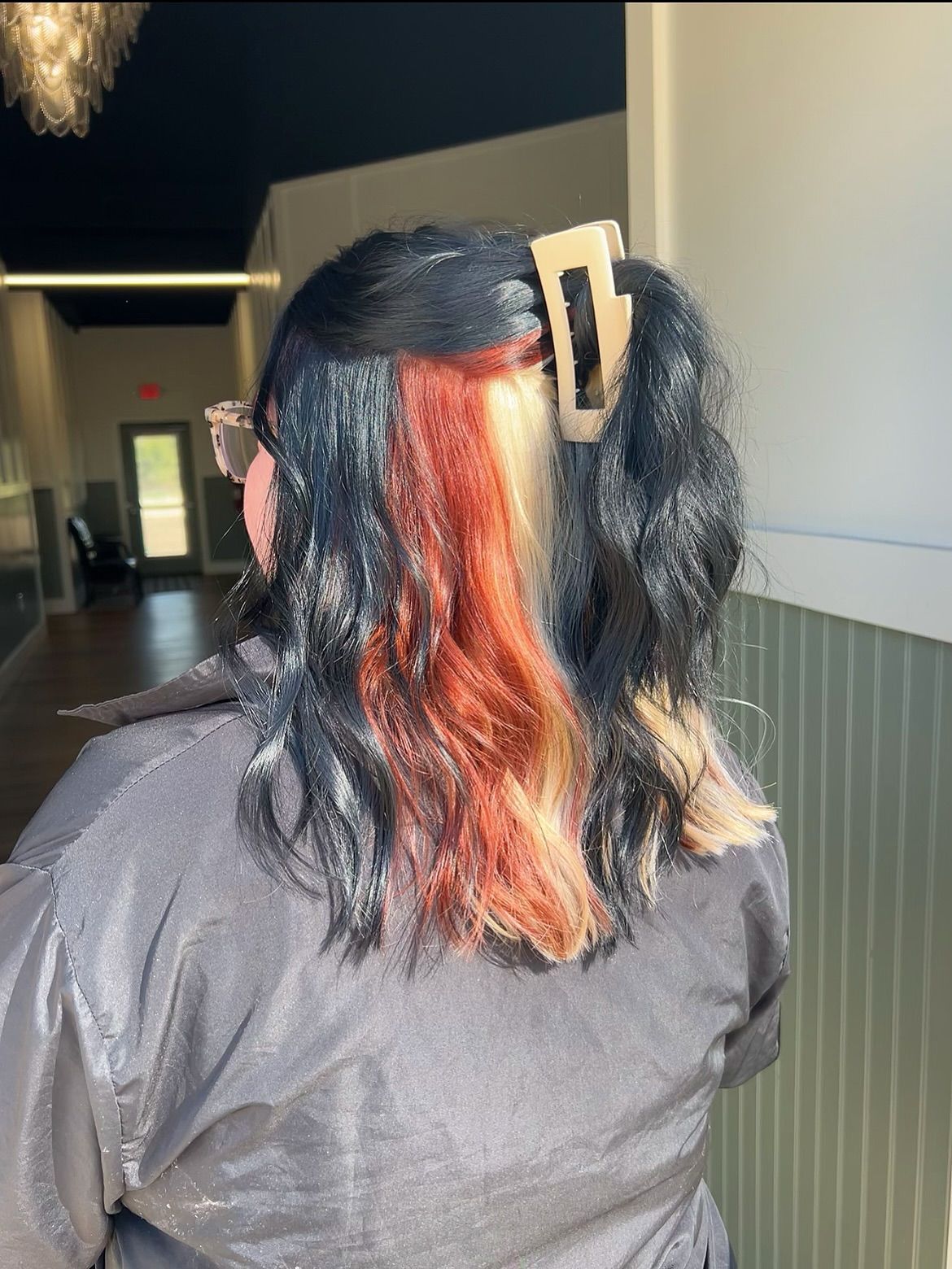 Person with black hair styled with a red and blonde streak, wearing a grey jacket, hair clip in.