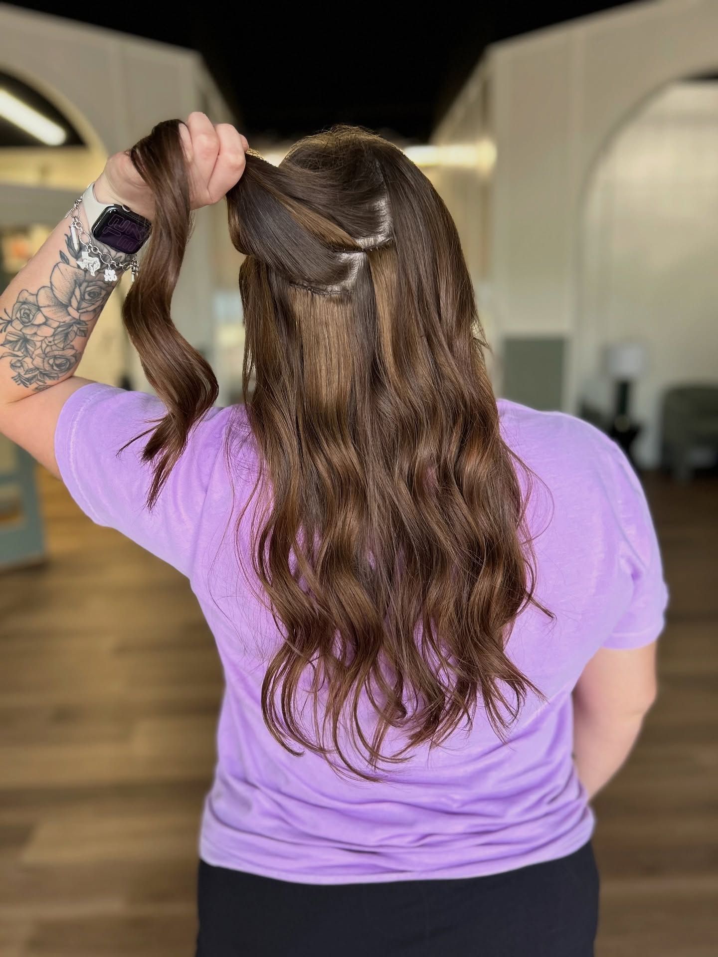 Woman with long brown hair, wearing a purple shirt, holding hair up to create a hairstyle.