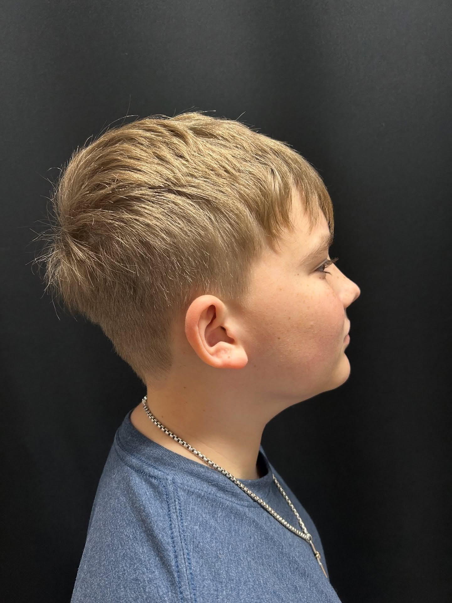 Boy with short, blonde hair, wearing a blue shirt, facing right against a black background.
