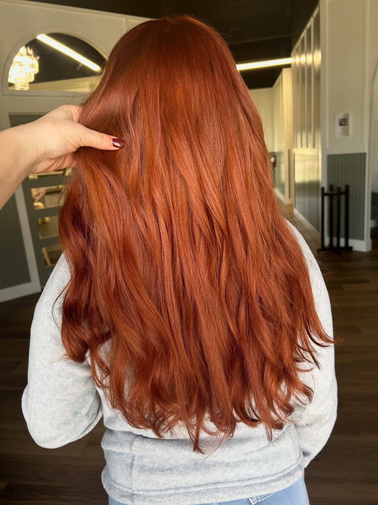 A person with long, auburn hair, styled with loose waves, has their hair being touched.