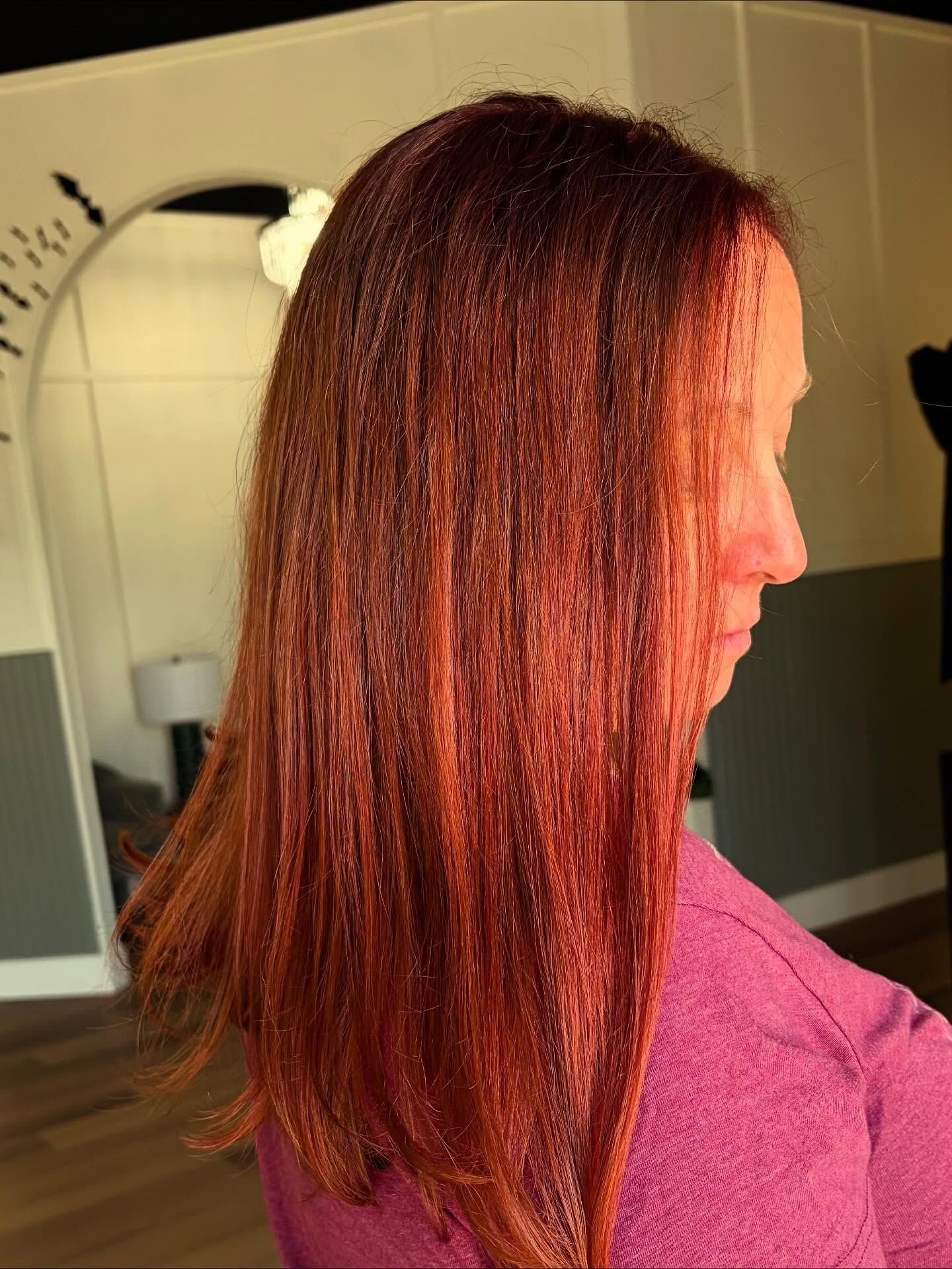 Woman with long, reddish-brown hair; in a salon setting, wearing a pink shirt.