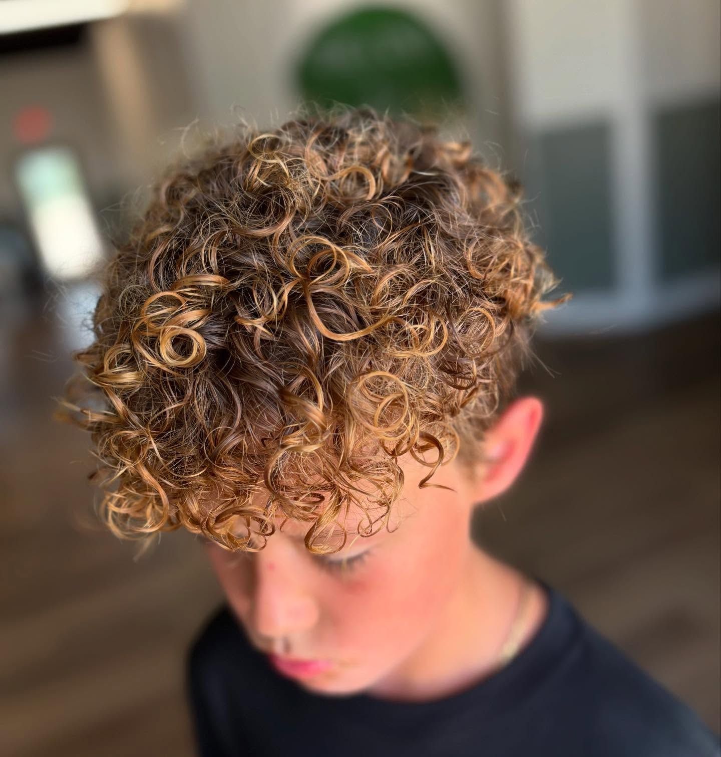 Boy with curly, highlighted hair, wearing a black shirt, looking down.