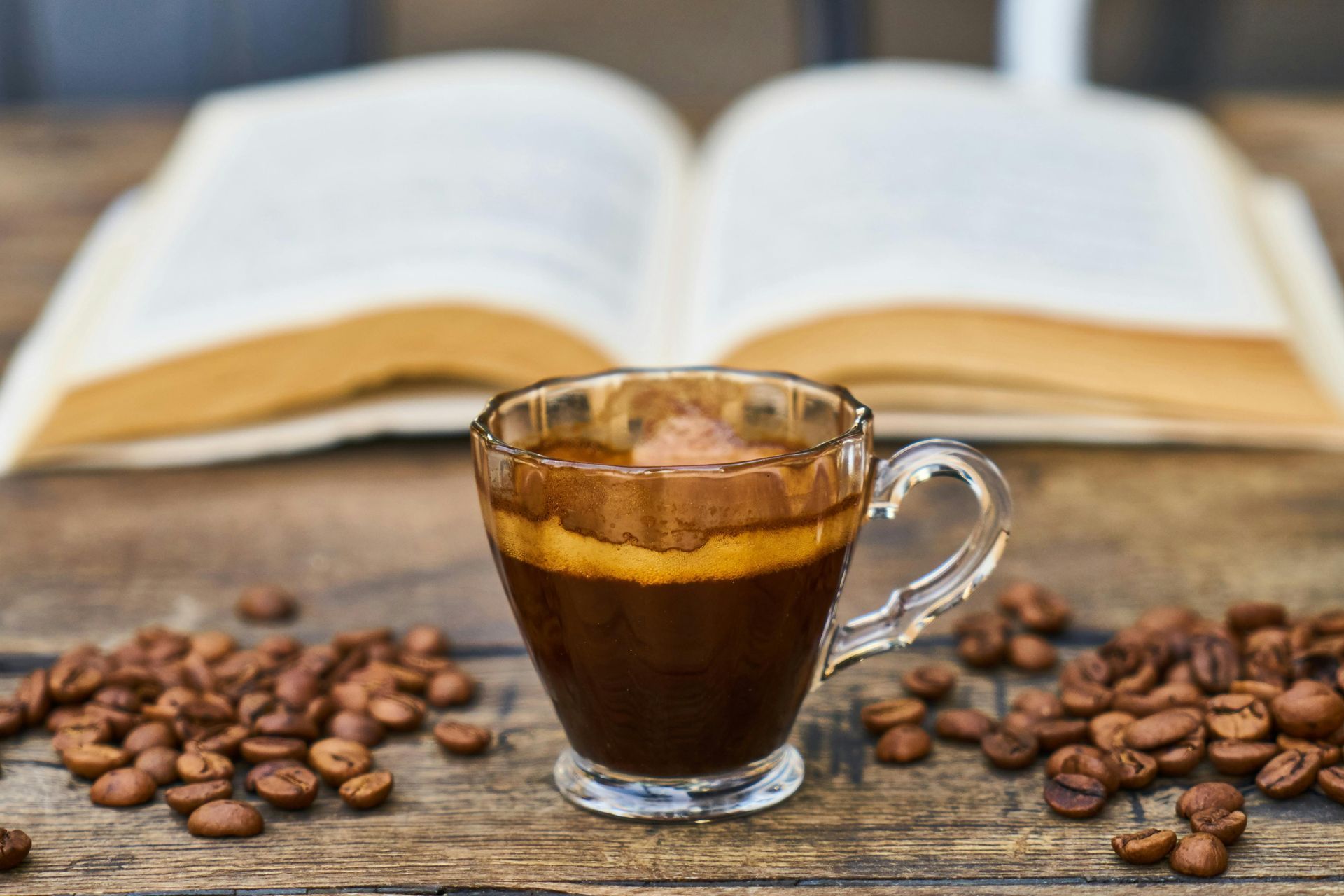 Cup of espresso, open book, and coffee beans on a wooden table.
