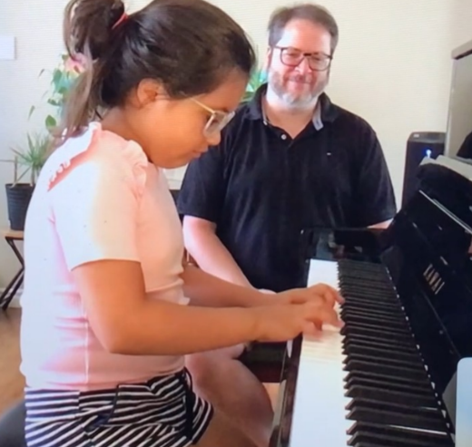 A young boy is sitting at a keyboard in front of a laptop computer.