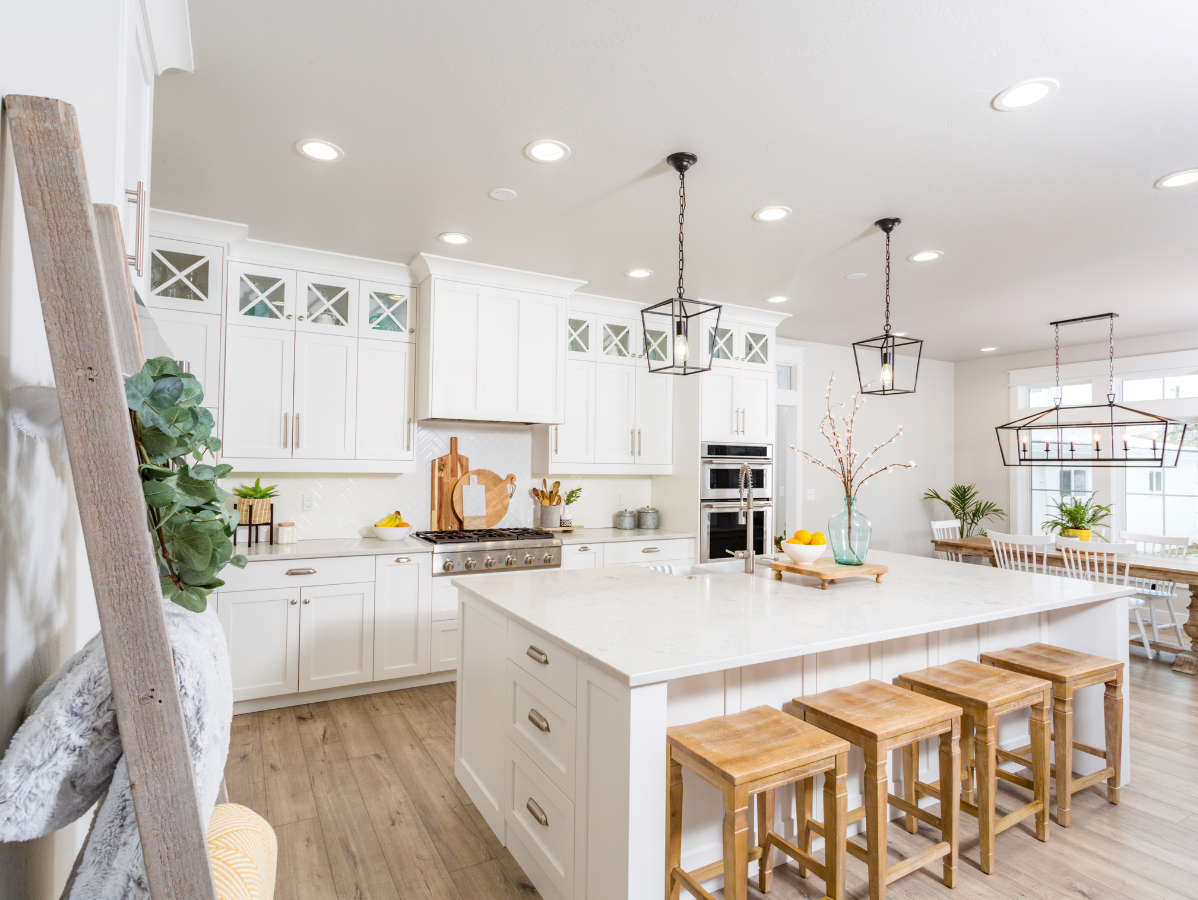 Bright white modern kitchen with island, wooden stools, pendant lights, and farmhouse decor.