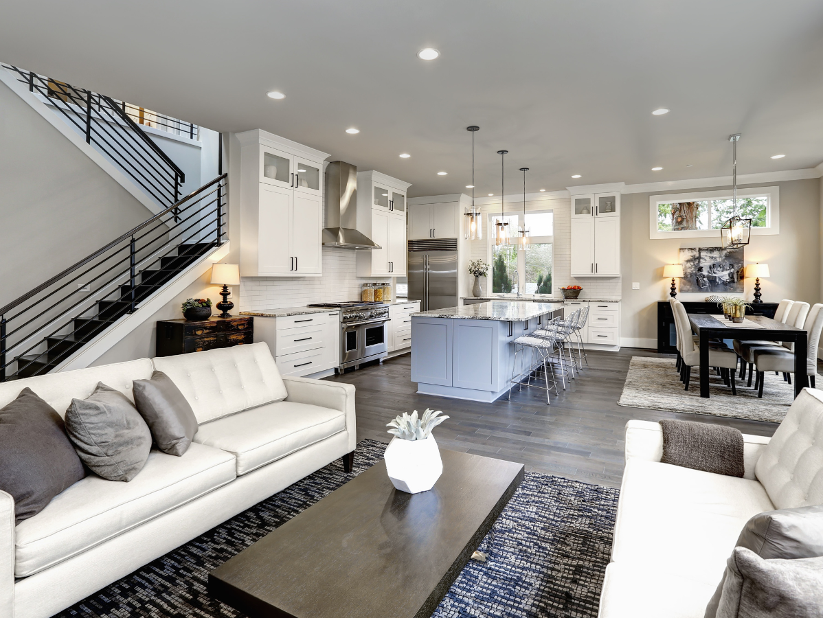Modern open-concept living room and kitchen with white furniture, gray accents, and a staircase.