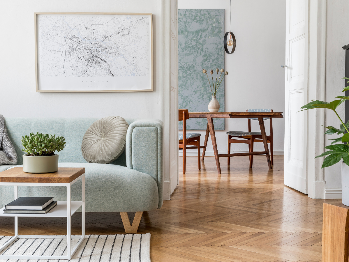 Bright living room with a mint sofa, wall art, wooden herringbone floor, and dining area beyond the doorway