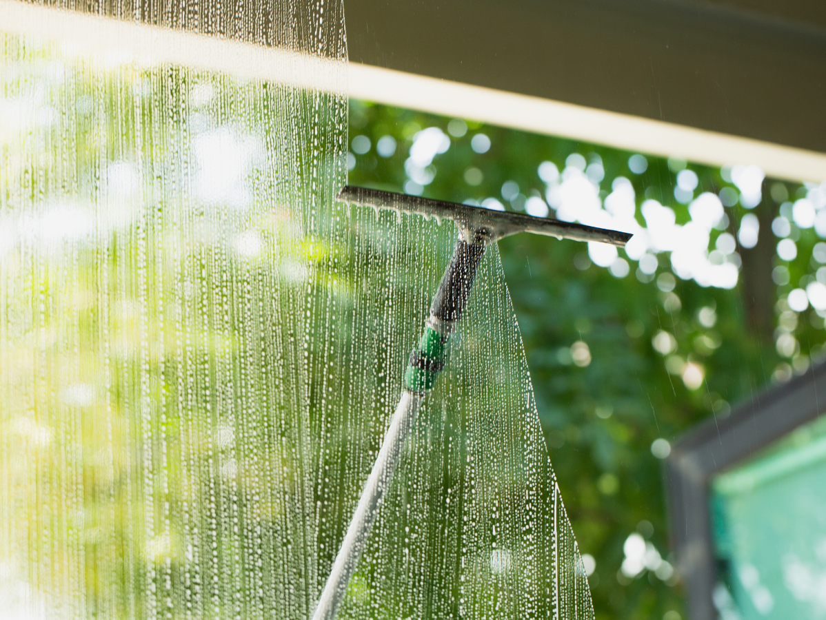 Sprinkler spraying water onto a glass panel outdoors with green trees in the background