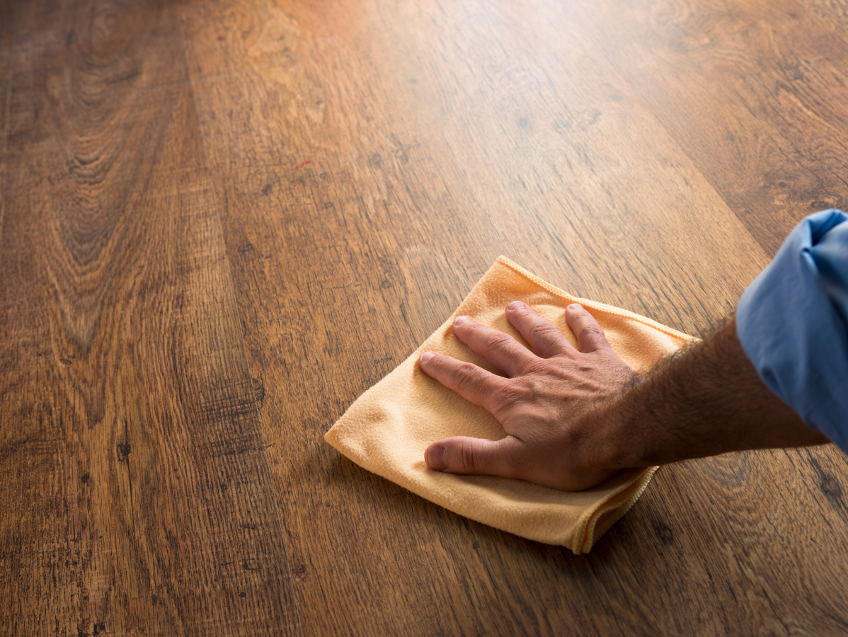 Hand wiping a wooden floor with a cloth, leaving a clean shine