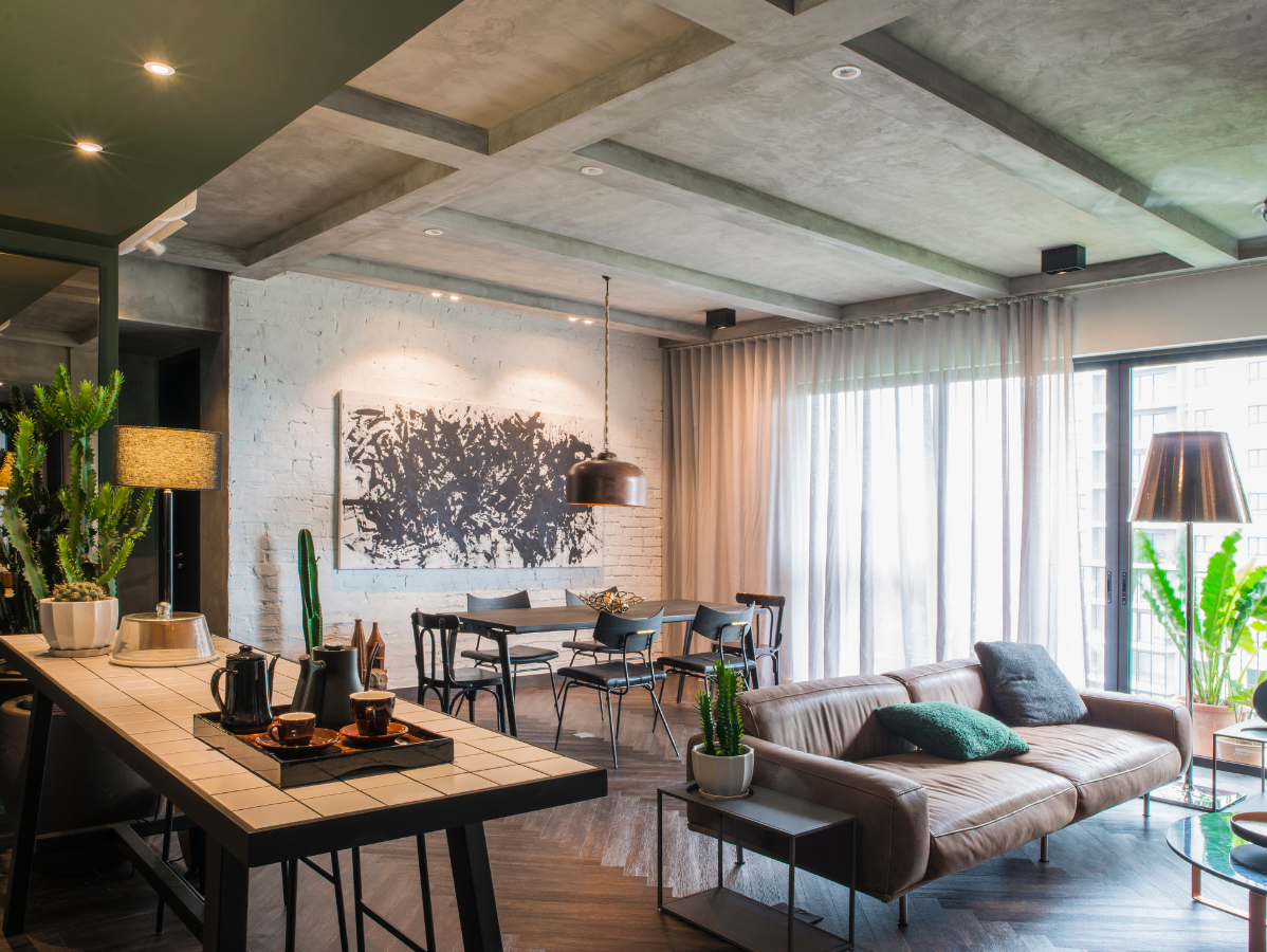 Modern open-plan living room with sofa, dining table, and large windows in a bright industrial loft
