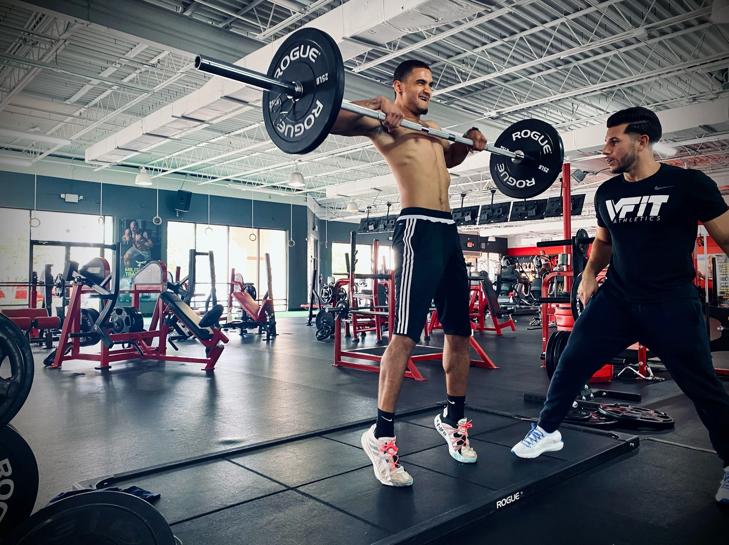 A man is lifting a barbell over his head in a gym.