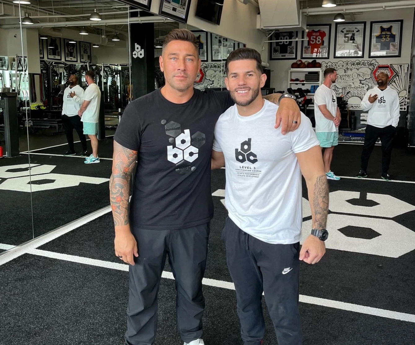 Two men are posing for a picture in a gym wearing black and white shirts