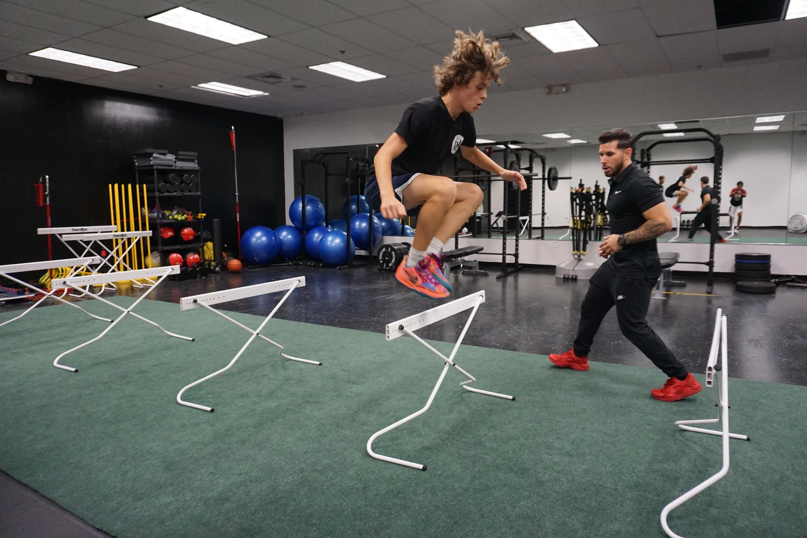 A man is helping a young boy jump over hurdles in a gym.