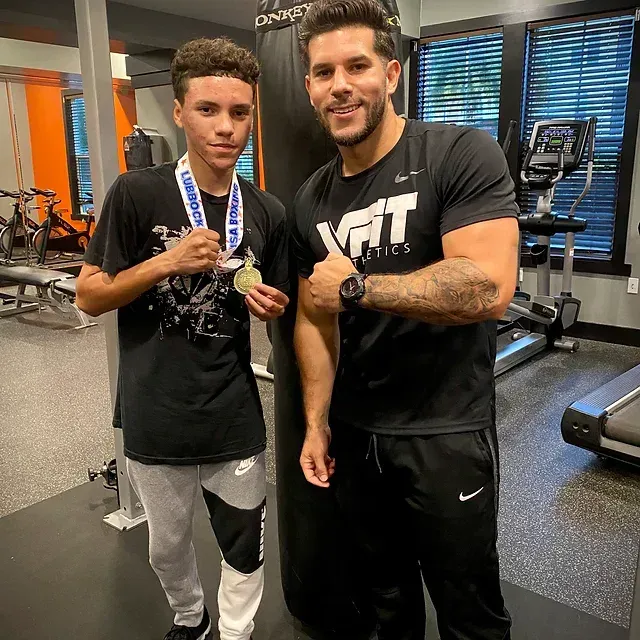 Two men are standing next to each other in a gym holding medals.
