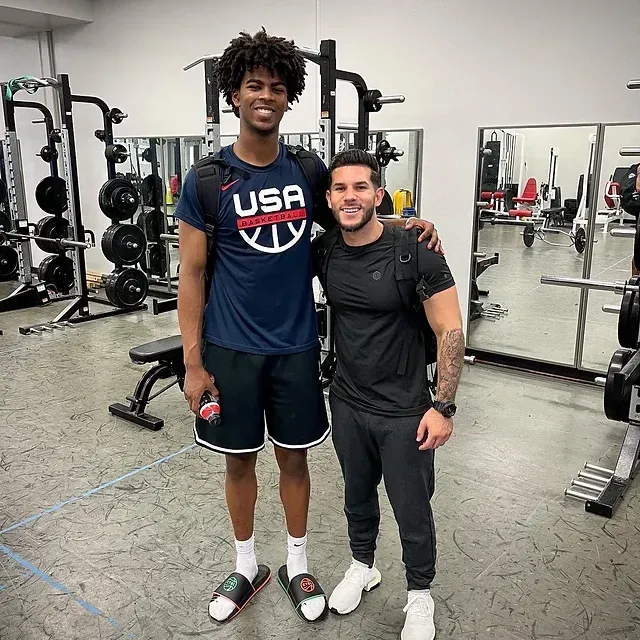 Two men are posing for a picture in a gym . one of the men is wearing a usa shirt.