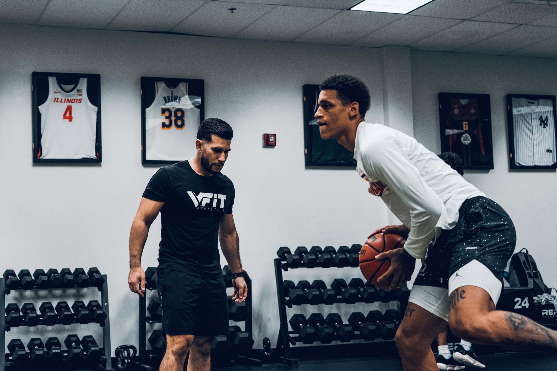 A man is teaching another man how to play basketball in a gym.