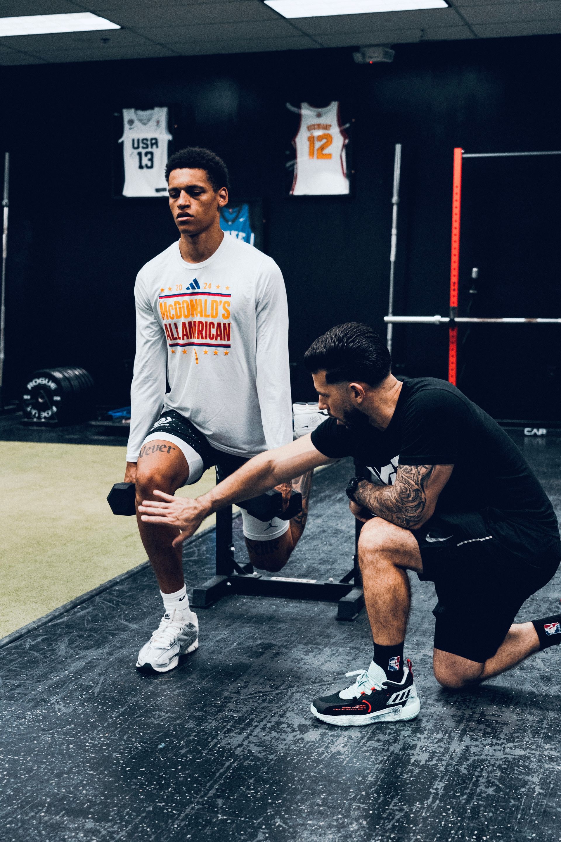 A man is helping another man do squats in a gym.