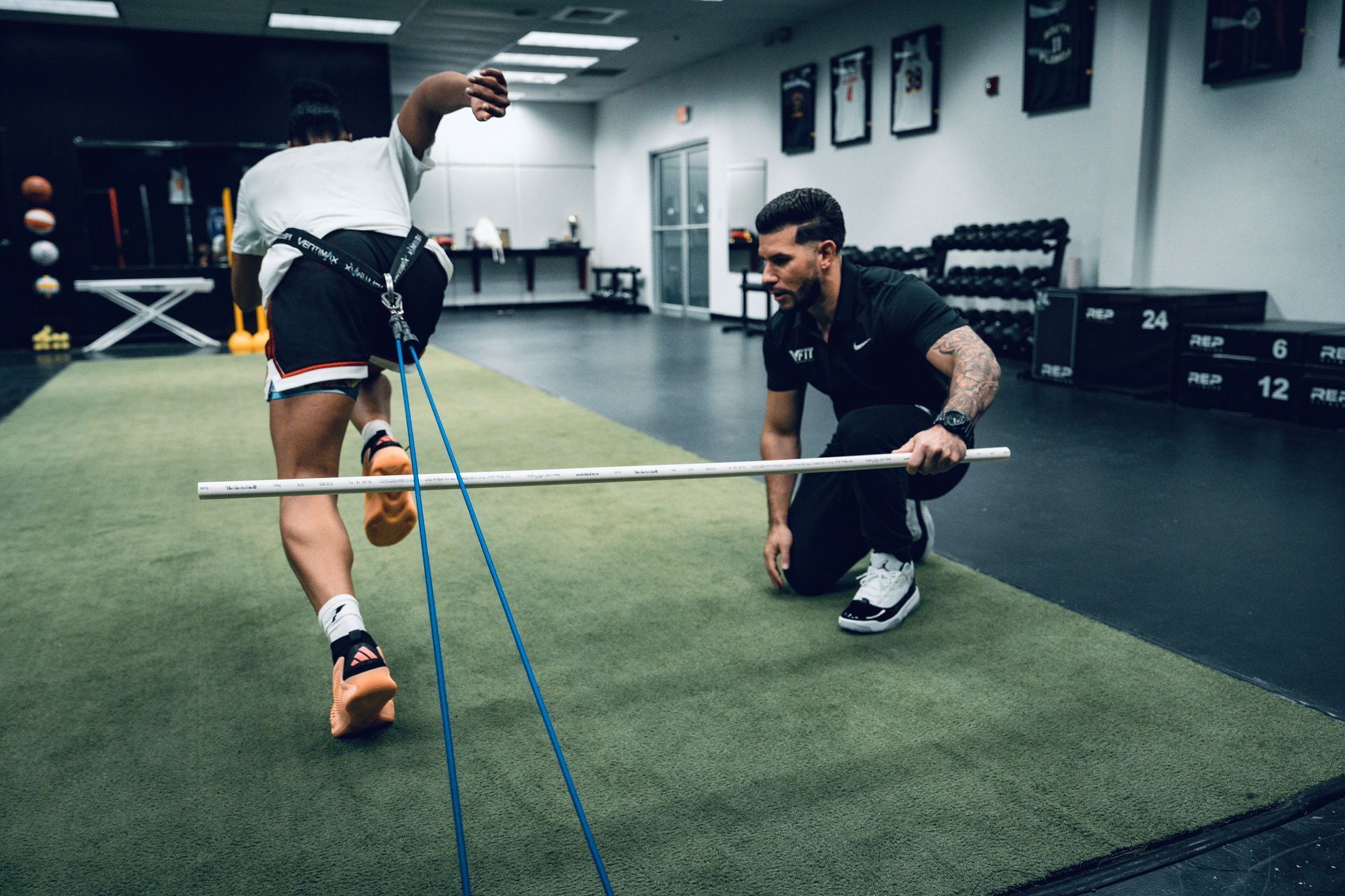 A man is kneeling down next to a person holding a bar in a gym.