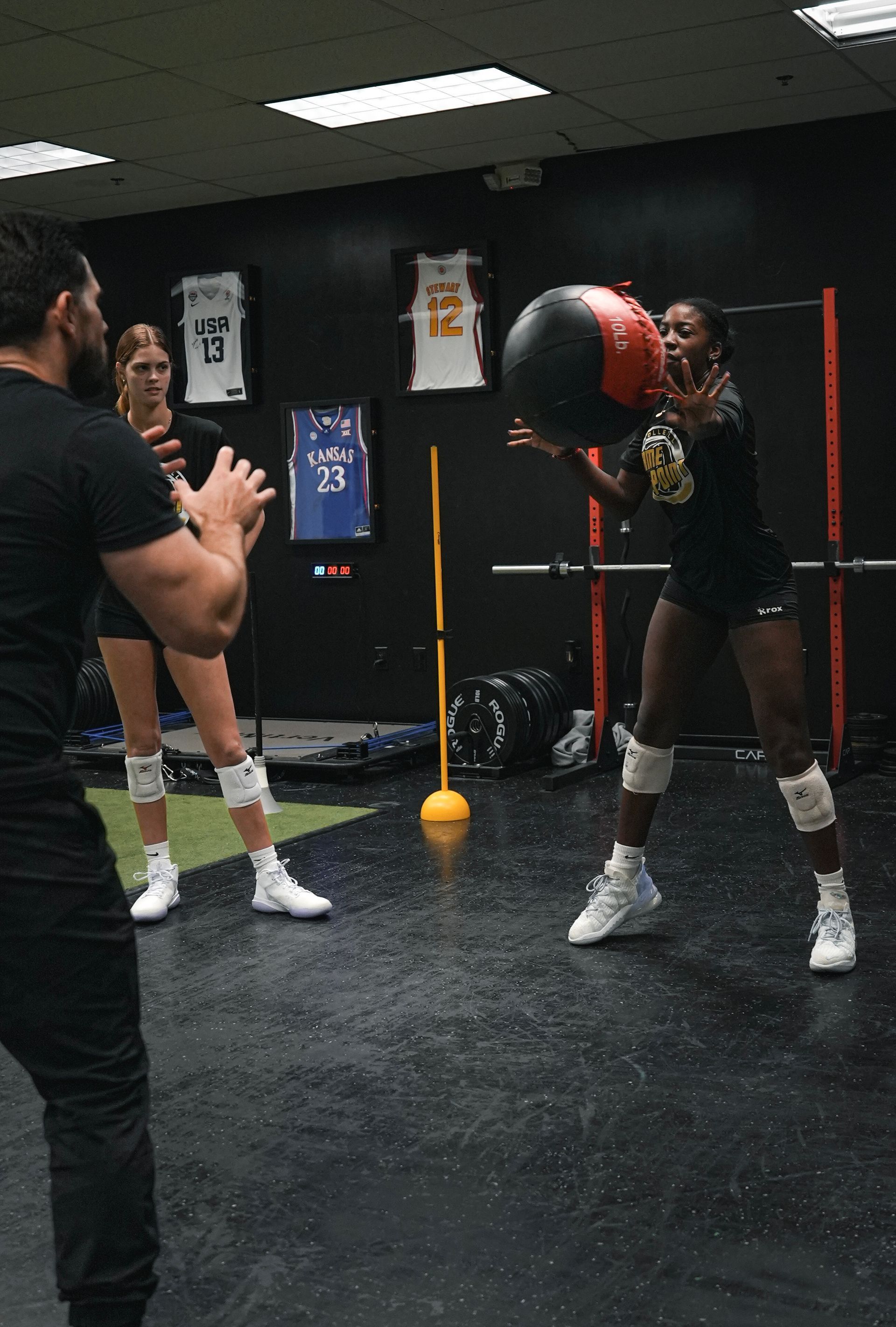 A man is standing next to a woman holding a medicine ball in a gym.