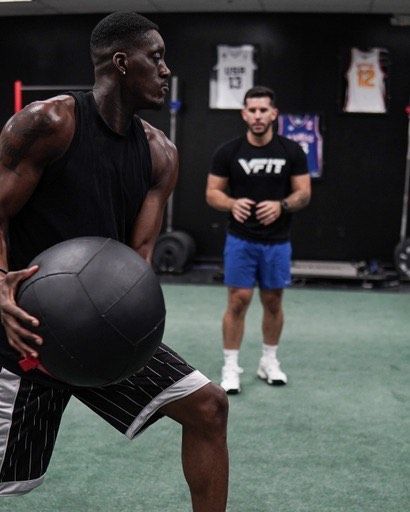 A man is holding a medicine ball in a gym while another man watches.