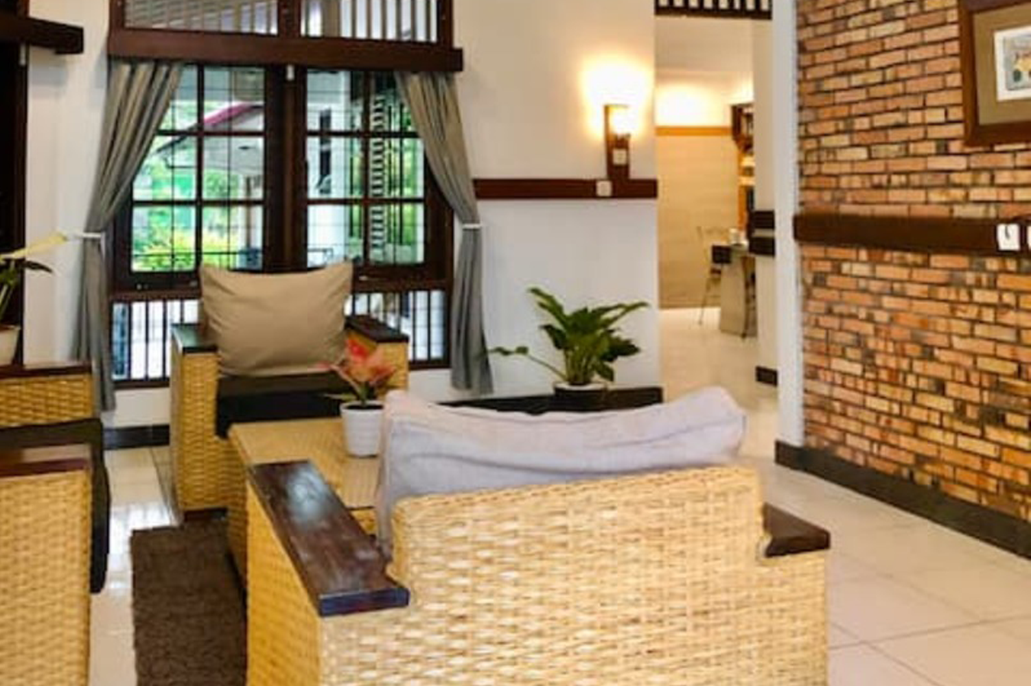Living room with wicker furniture, a brick wall, and a window with green view.