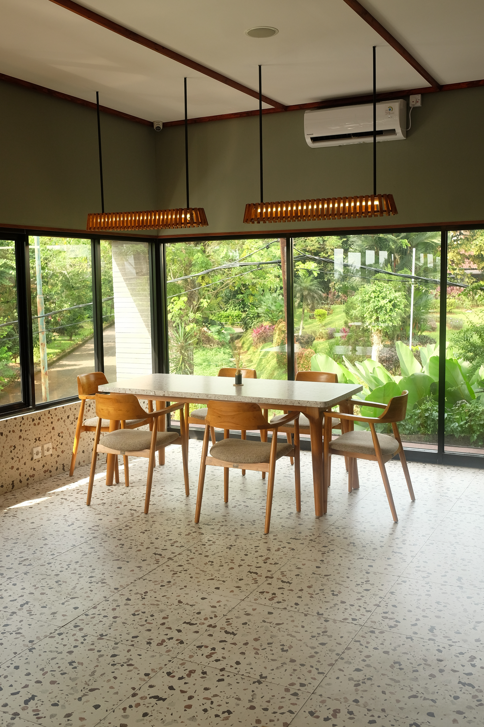 Dining room with table and chairs. Large windows offer a view of greenery. Decorative lighting.