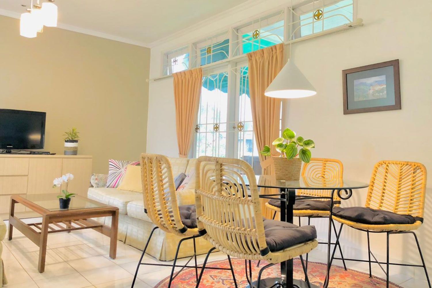 Living room with dining area: cream couch, rattan chairs, round glass table, and beige walls.