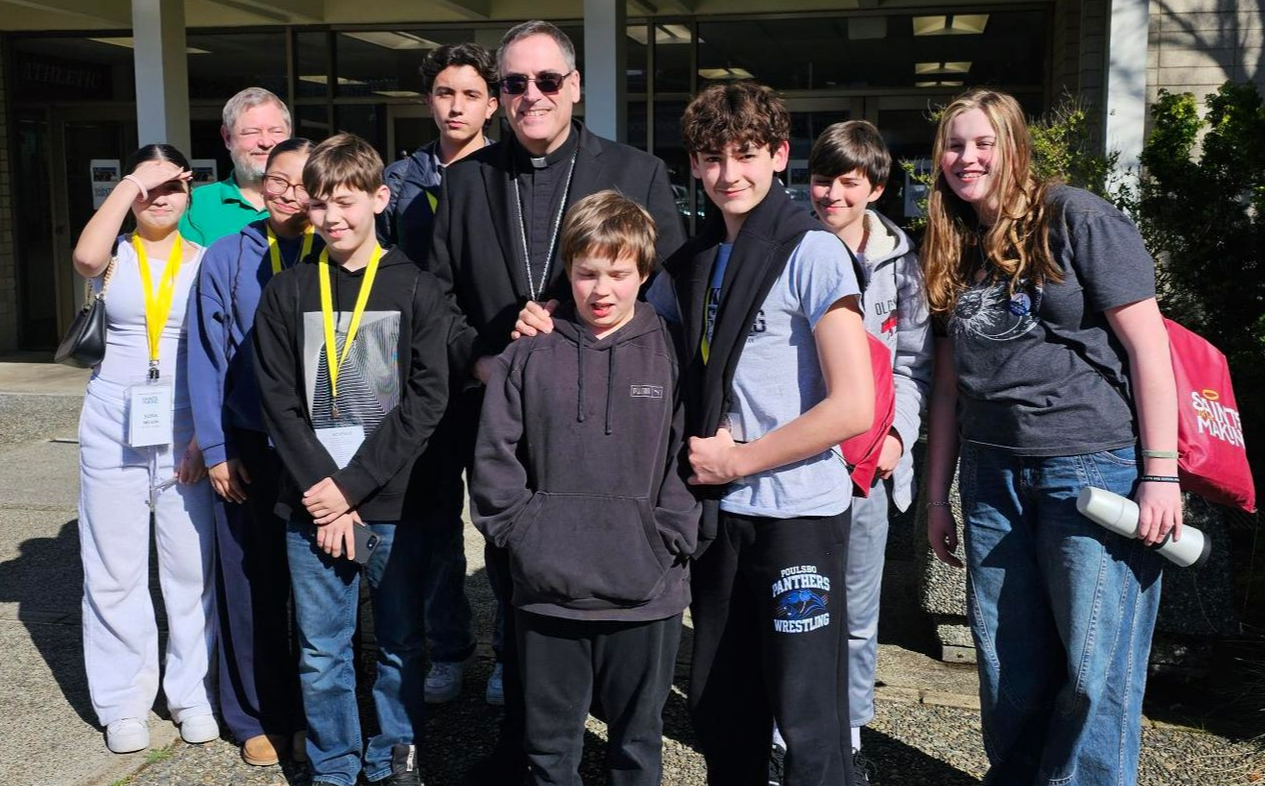 Group of youth standing outside a building, some smiling and wearing backpacks and lanyards.