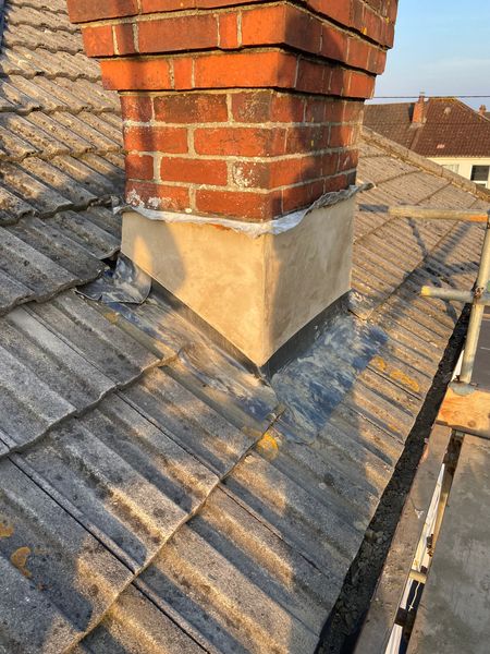 A brick chimney is sitting on top of a tiled roof.