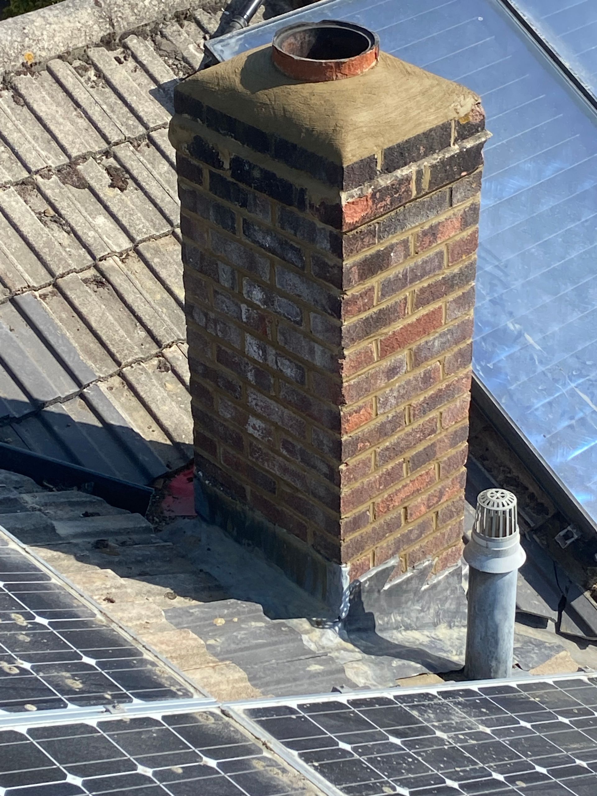 A brick chimney is sitting on top of a roof next to solar panels.