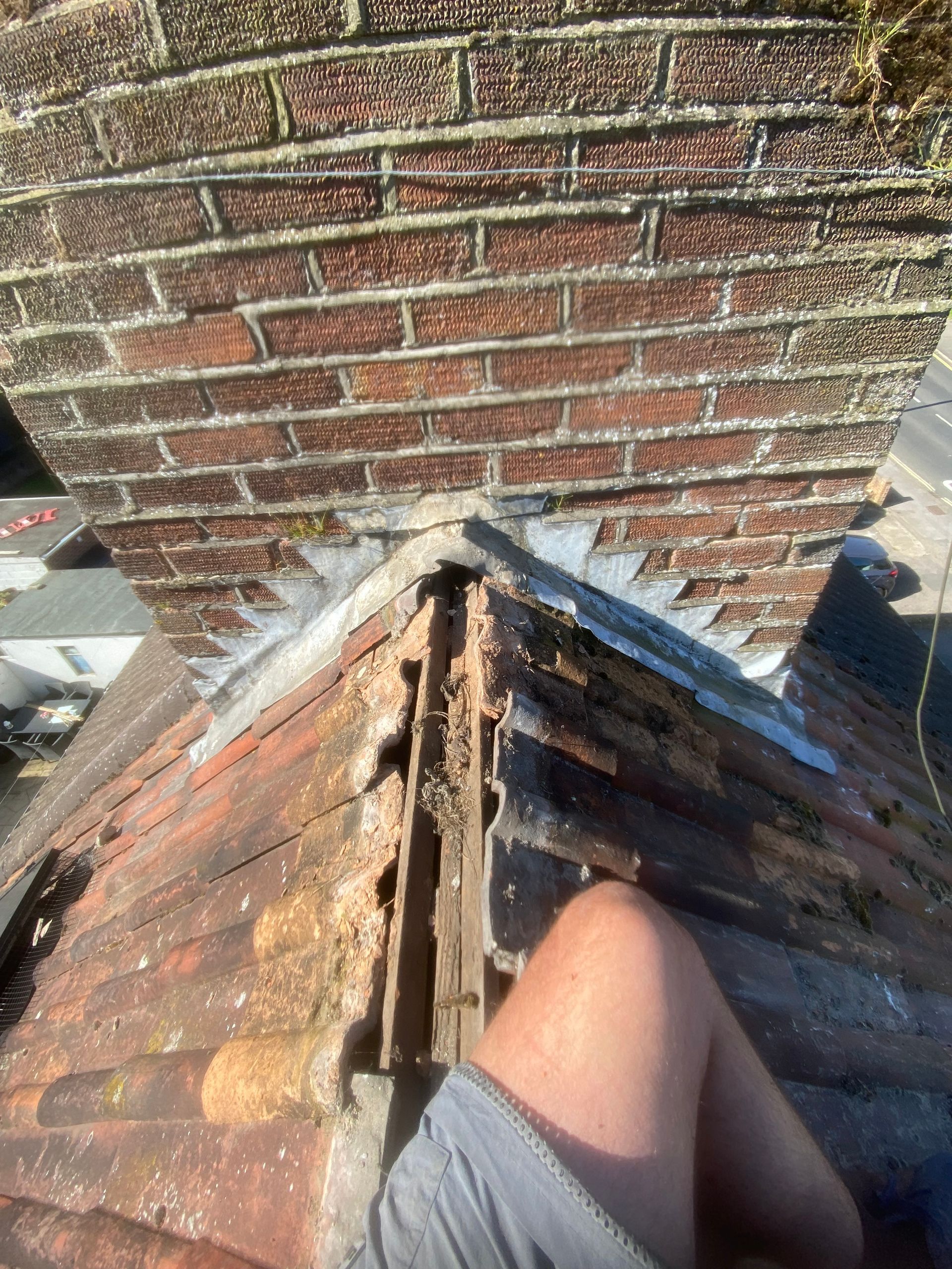 A person is sitting on top of a roof next to a brick chimney.