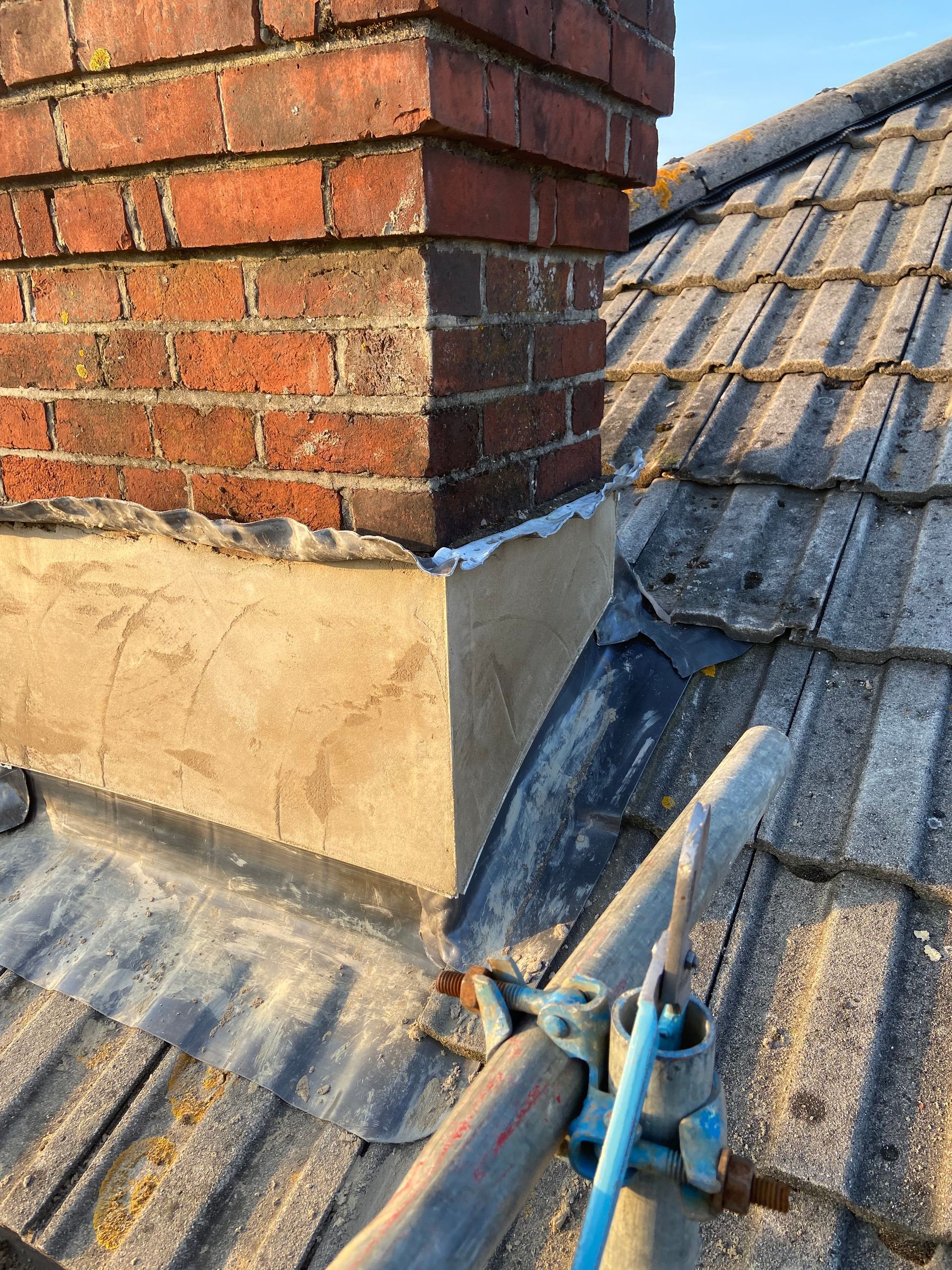 A brick chimney is sitting on top of a tiled roof.