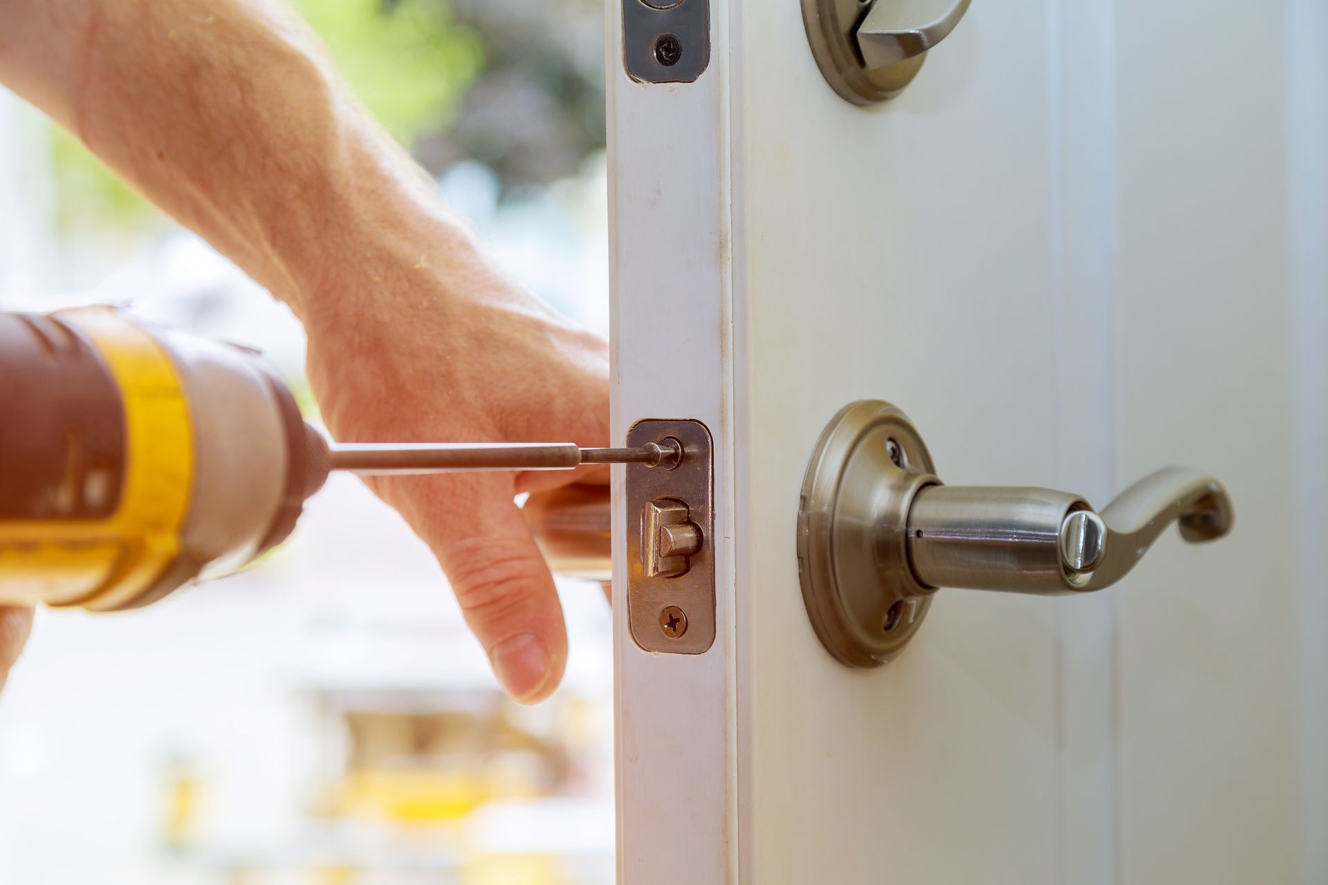 A person is using a screwdriver to repair the door handle and latch mechanism.