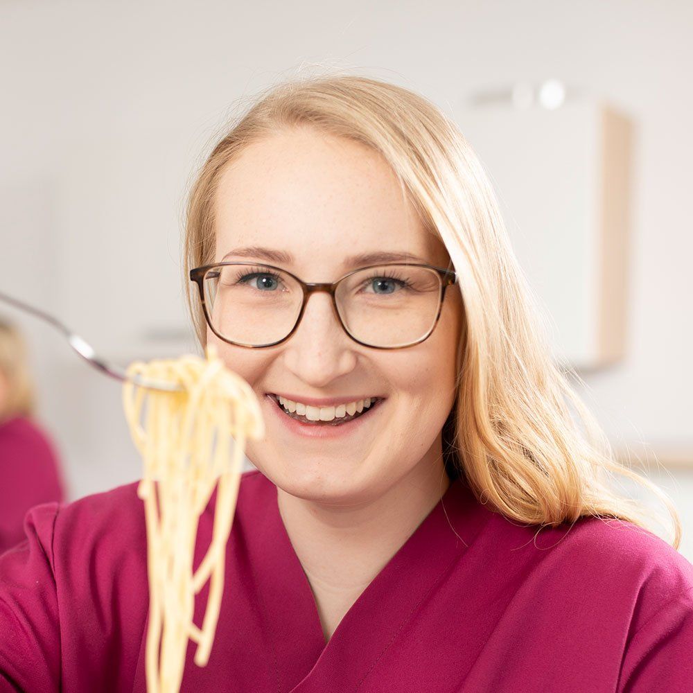 Eine Pflegekraft von careVitaale hält strählend eine Gabel mit Spaghetti in die Kamera.