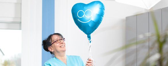 Eine Pflegekraft hält einen blauen careVitaale Herz-Luftballon in der Hand und lächelt ihn an.