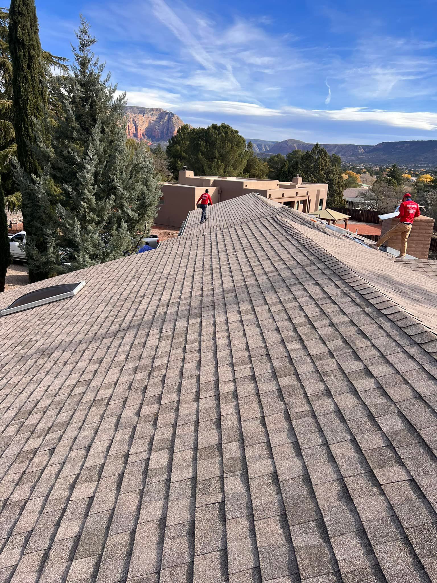 Workers on a rooftop installing shingles, scenic view of mountains in the background, clear blue sky.