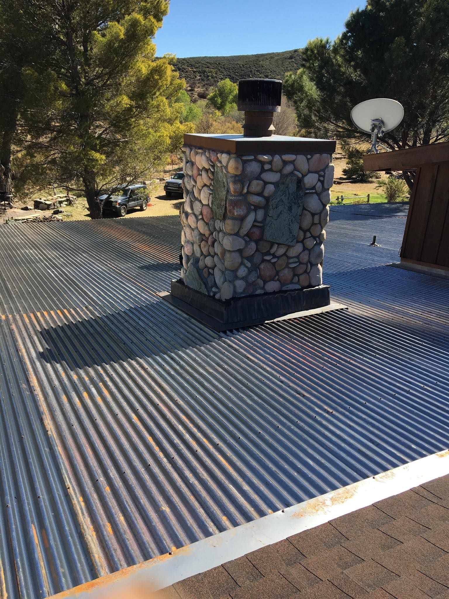 Stone chimney on corrugated metal roof; trees and landscape in the background.