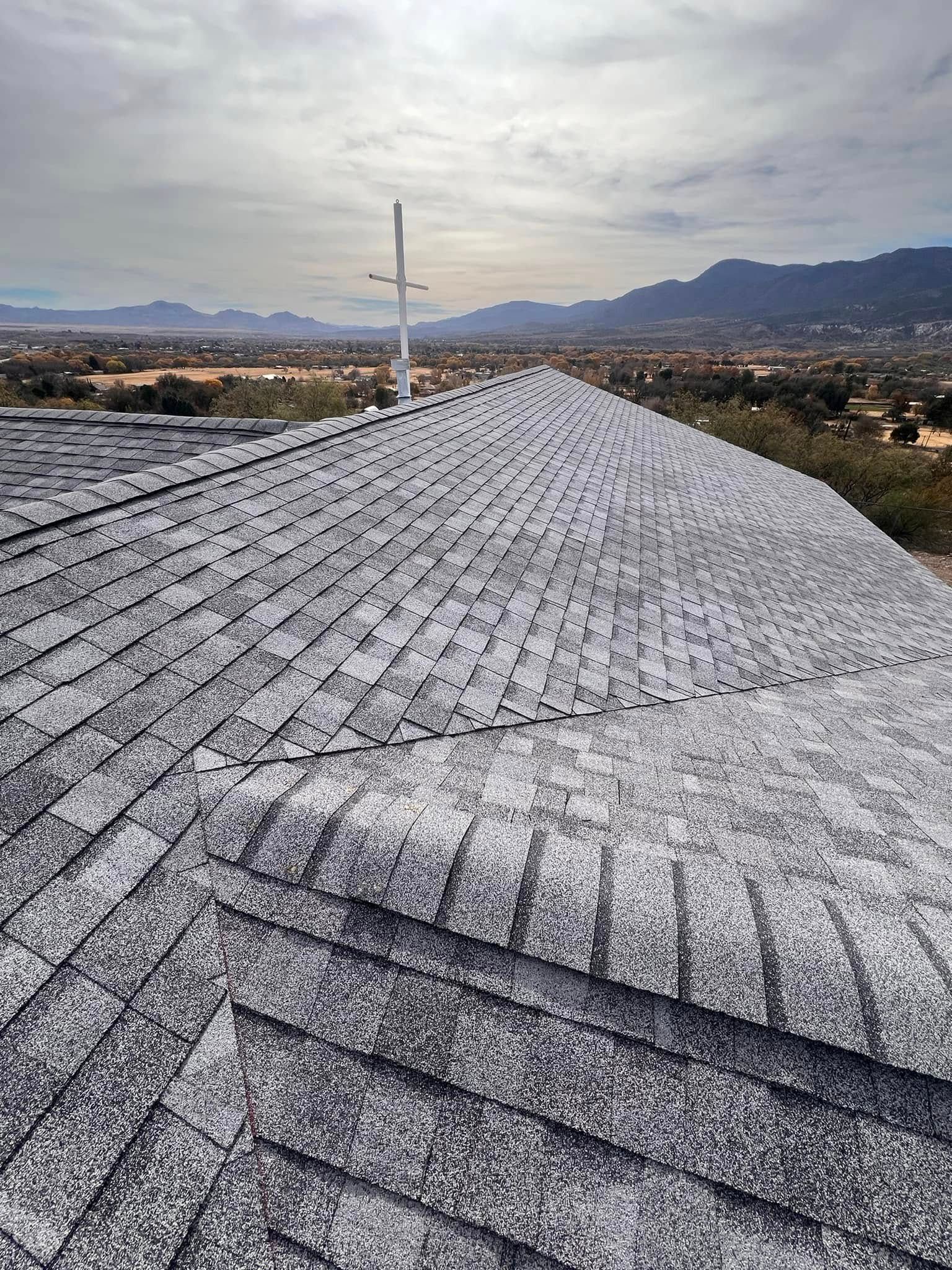 Gray shingled roof with a central ridge, antenna, and desert landscape in the background under a cloudy sky.
