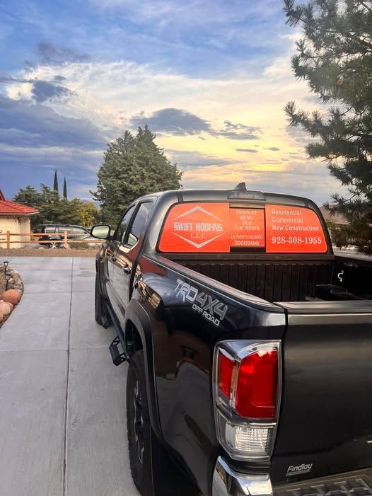 Black Toyota Tacoma truck parked in a driveway with business advertisement on the back window. Sunset sky.