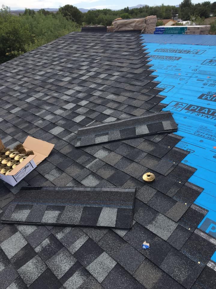 Roofers installing asphalt shingles on a roof, partially complete. Blue underlayment exposed.